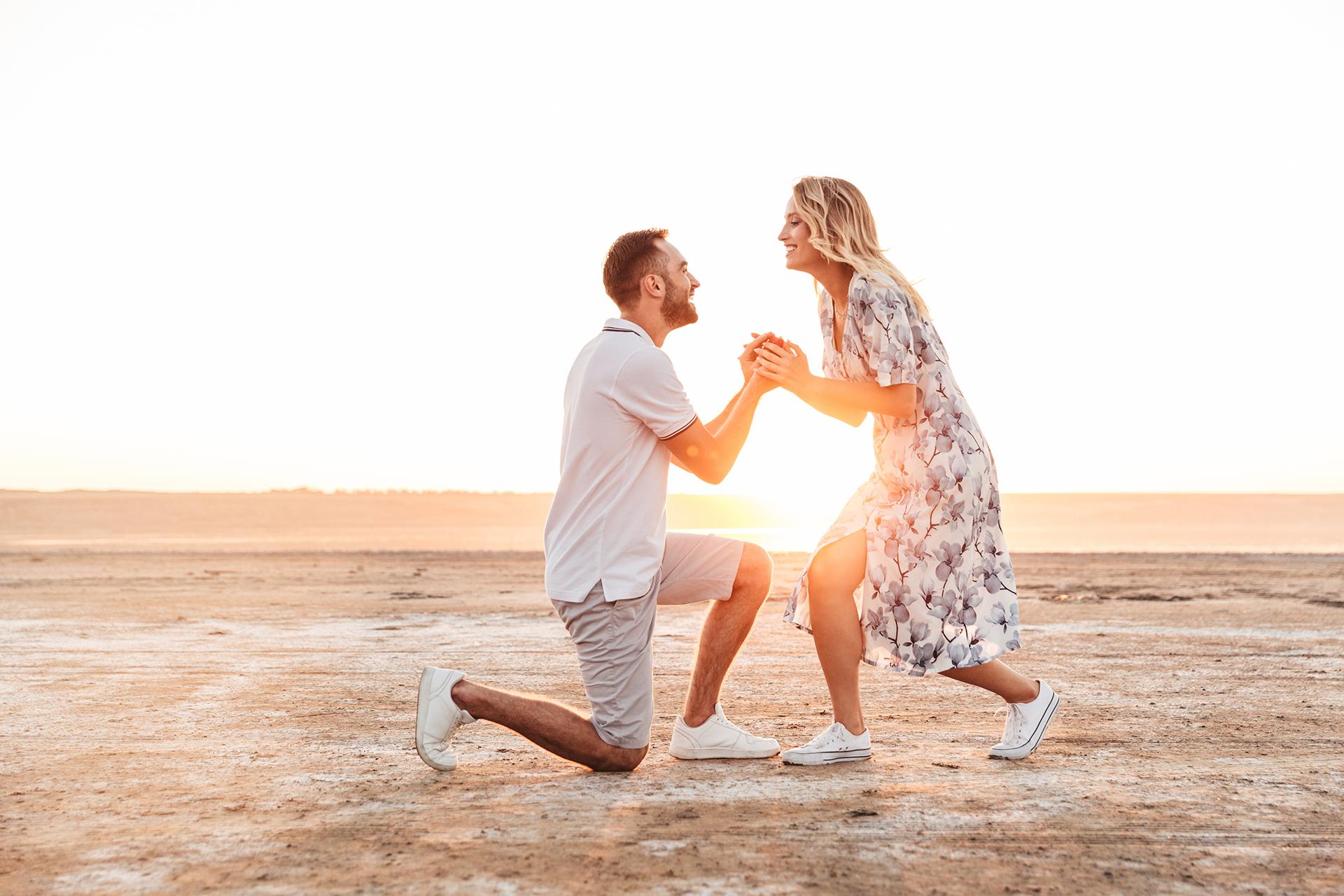 Photo of happy man making proposal to his delighted woman with ring while walking on sunny beach Engagement Photography